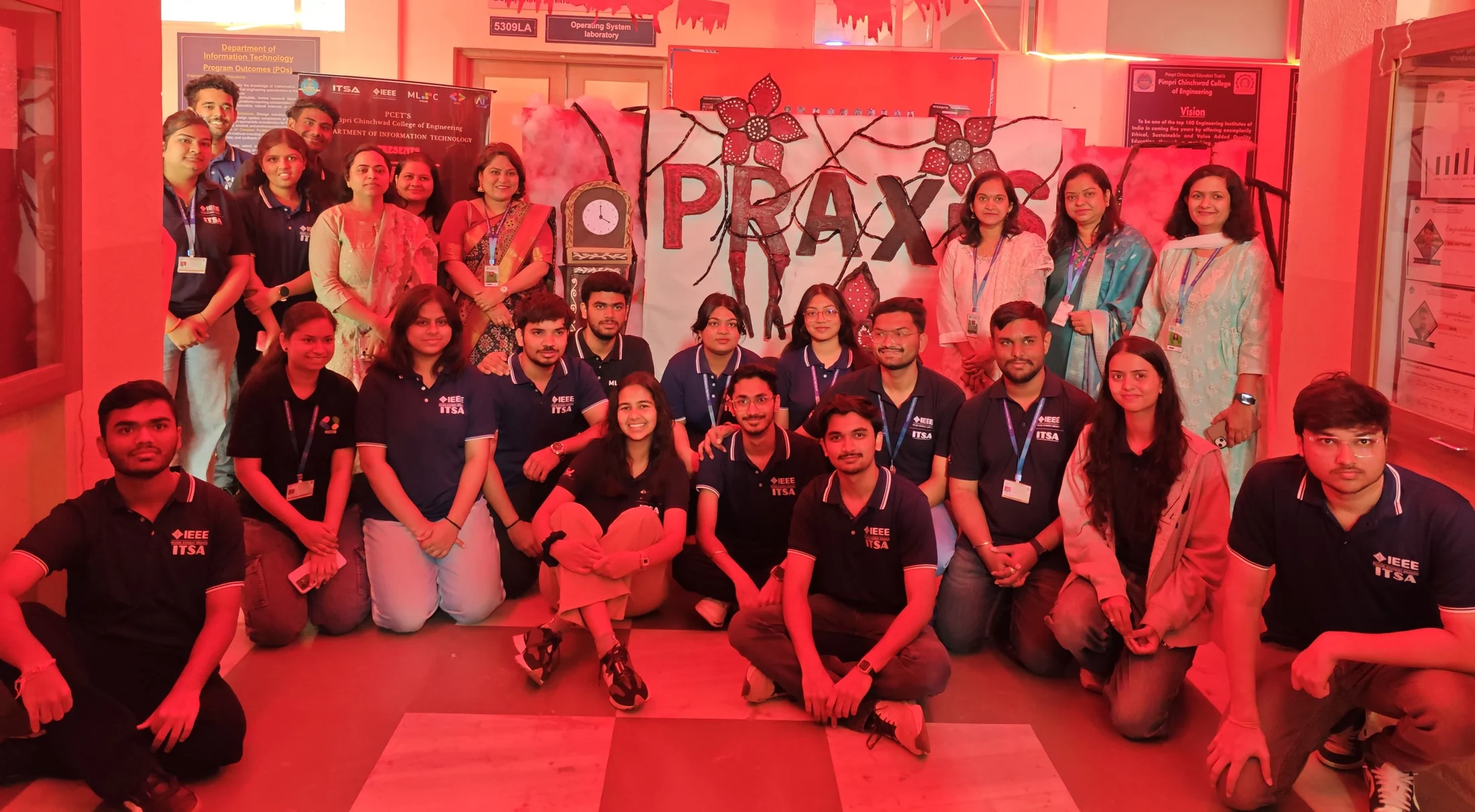 A large group posing in front of a Praxis display in a room with red lighting