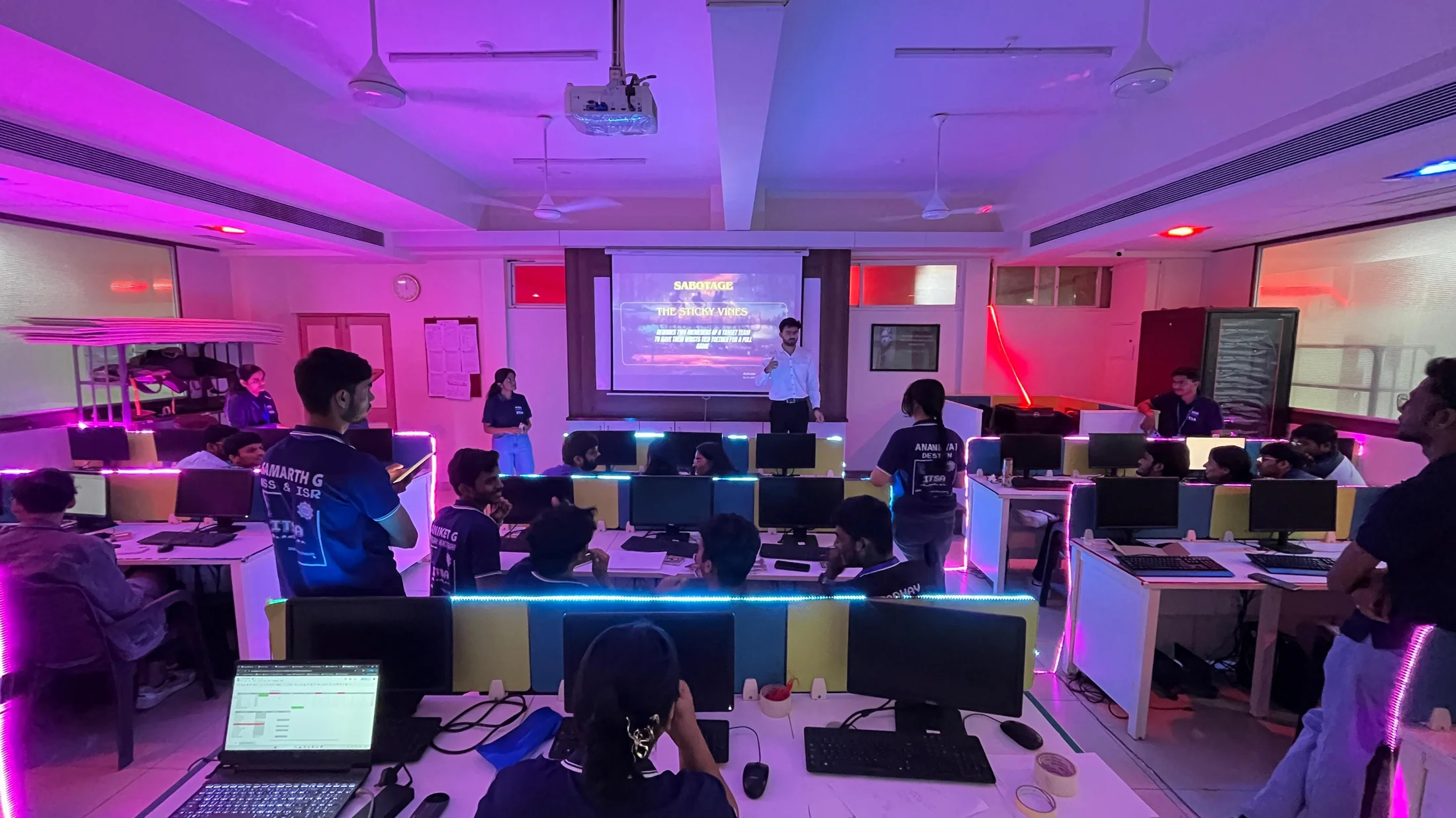 Participants working at computer stations in a room illuminated with purple and red lights
