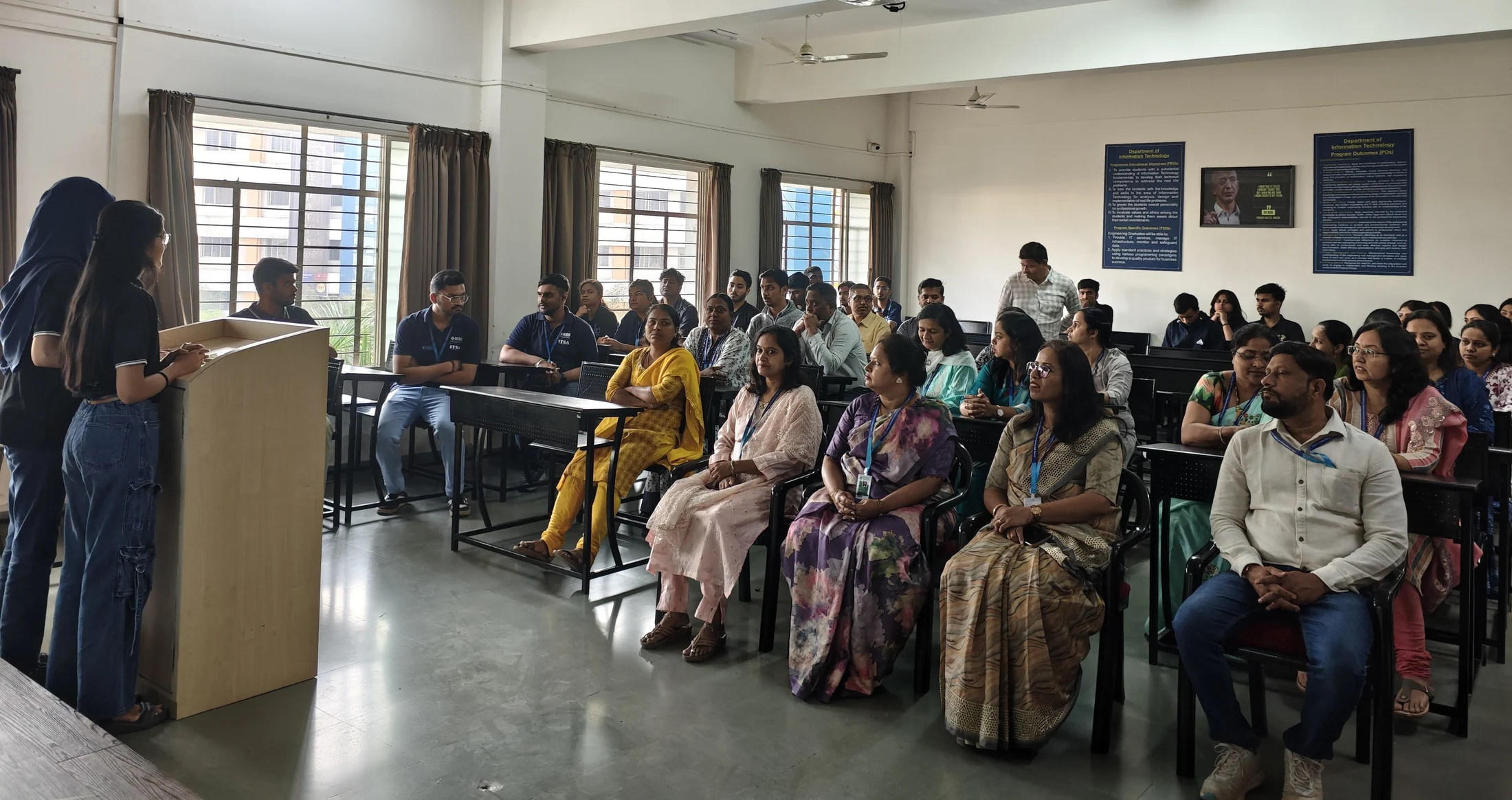 An audience seated in a classroom watching a speaker at a lectern